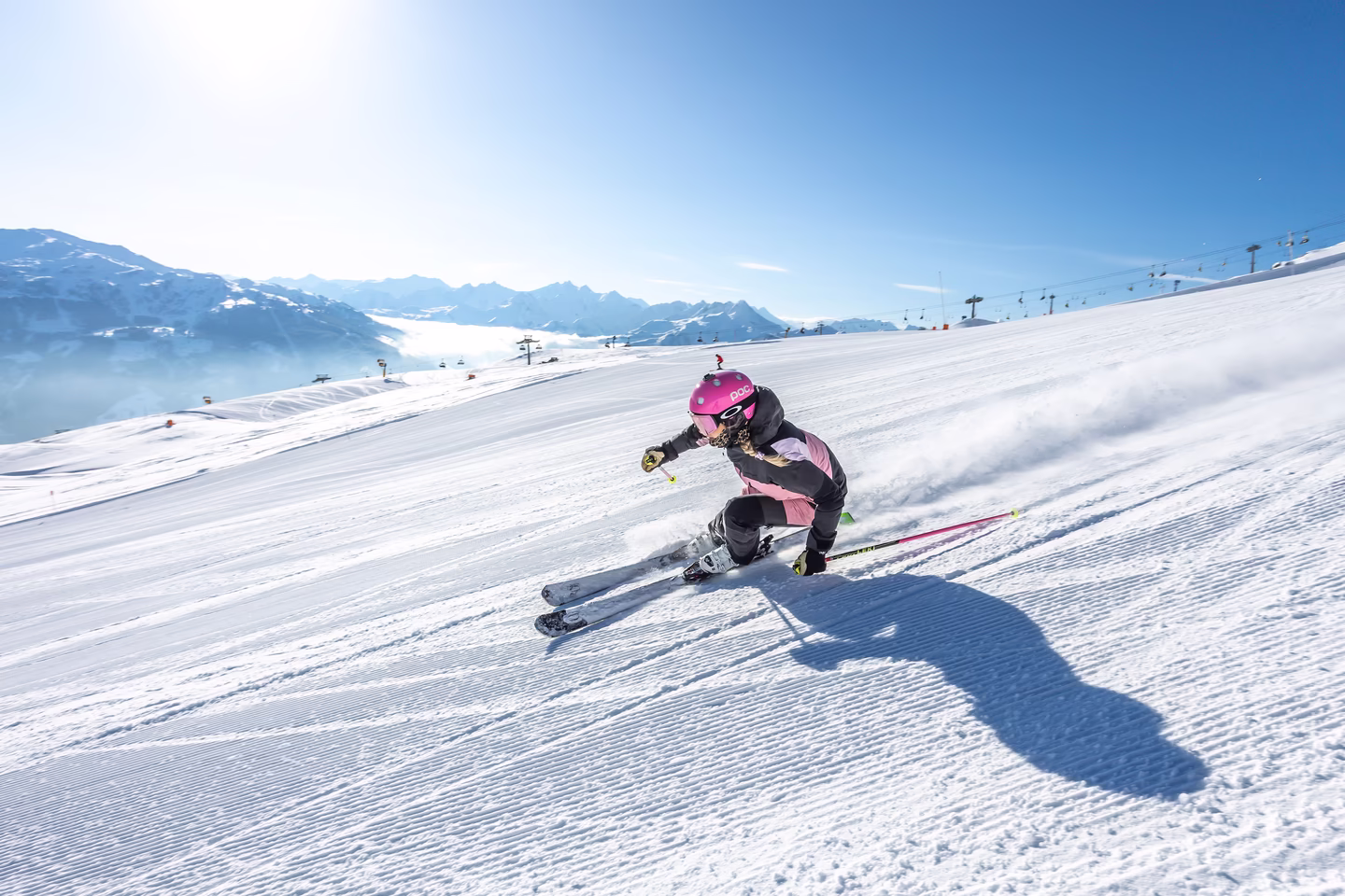 Frau mit pinkem Helm fährt dynamisch Ski auf frisch präparierter Piste vor Bergpanorama im Skigebiet Hochzillertal.